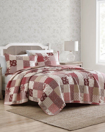 Celina Patchwork Cranberry Cotton Reversible Quilt Set angle view of quilt and shams on a bed